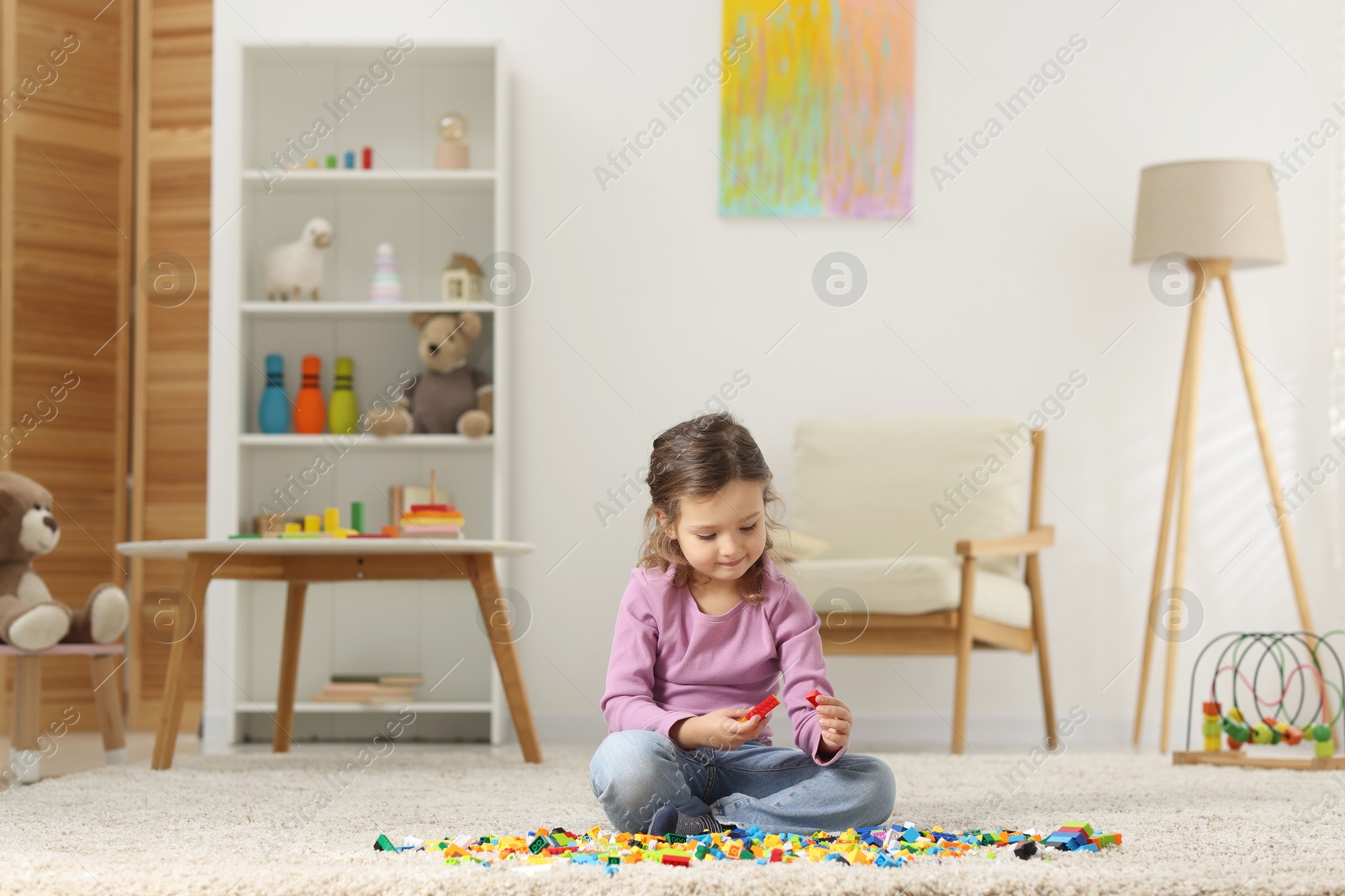 Photo of Cute girl playing with building blocks on floor at home