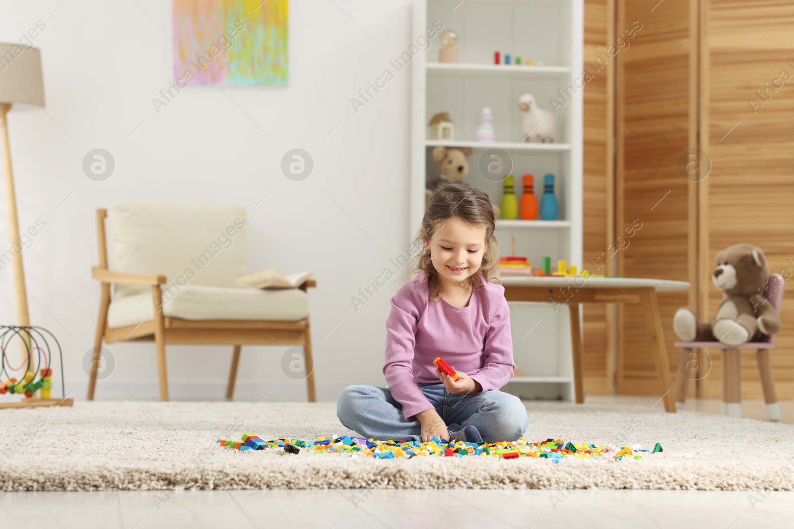 Photo of Cute girl playing with building blocks on floor at home. Space for text