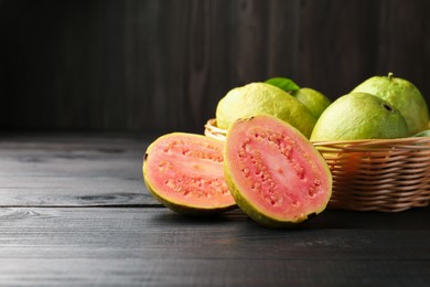 Photo of Fresh whole and cut guava fruits on black wooden table, space for text