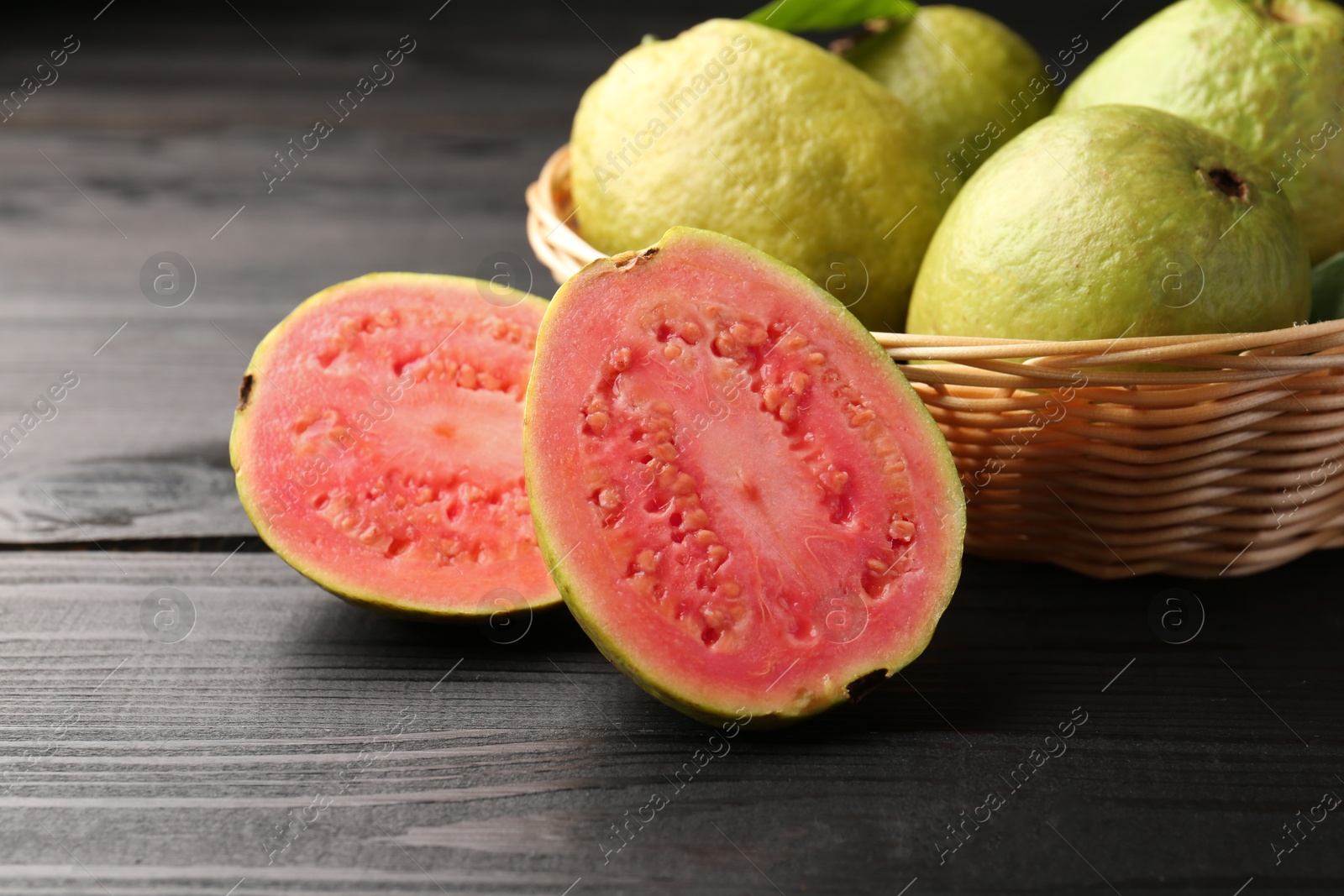 Photo of Fresh whole and cut guava fruits on black wooden table, closeup