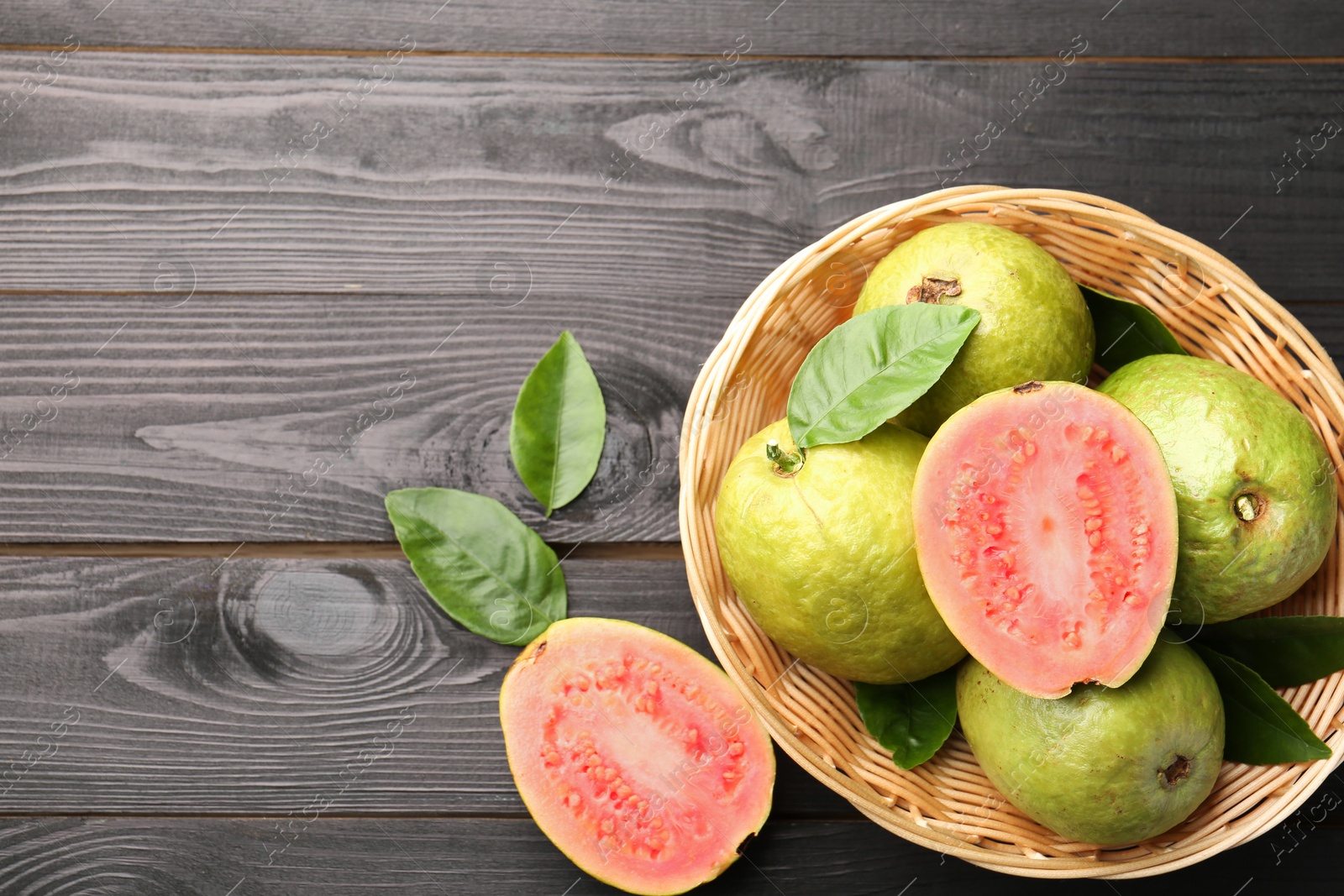 Photo of Fresh whole and cut guava fruits on black wooden table, flat lay. Space for text