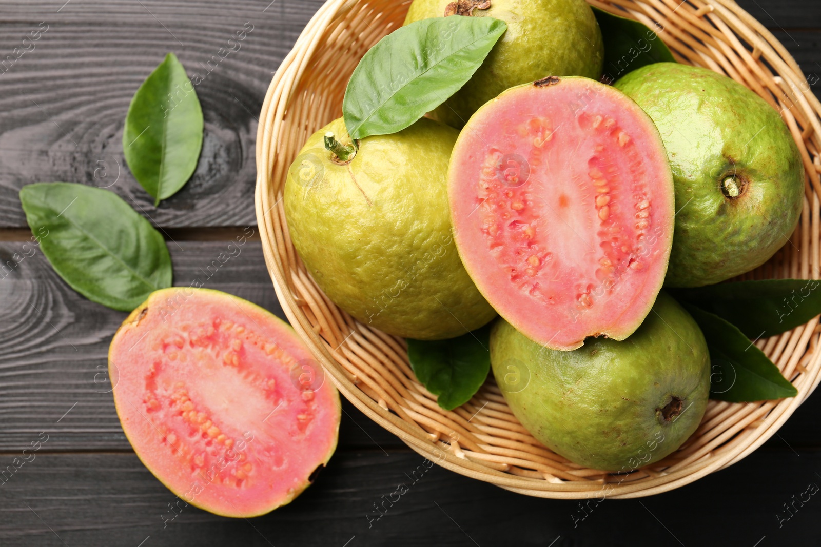 Photo of Fresh whole and cut guava fruits on black wooden table, flat lay