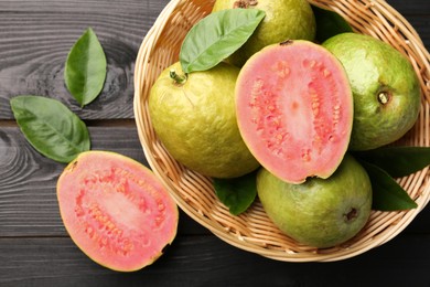 Fresh whole and cut guava fruits on black wooden table, flat lay