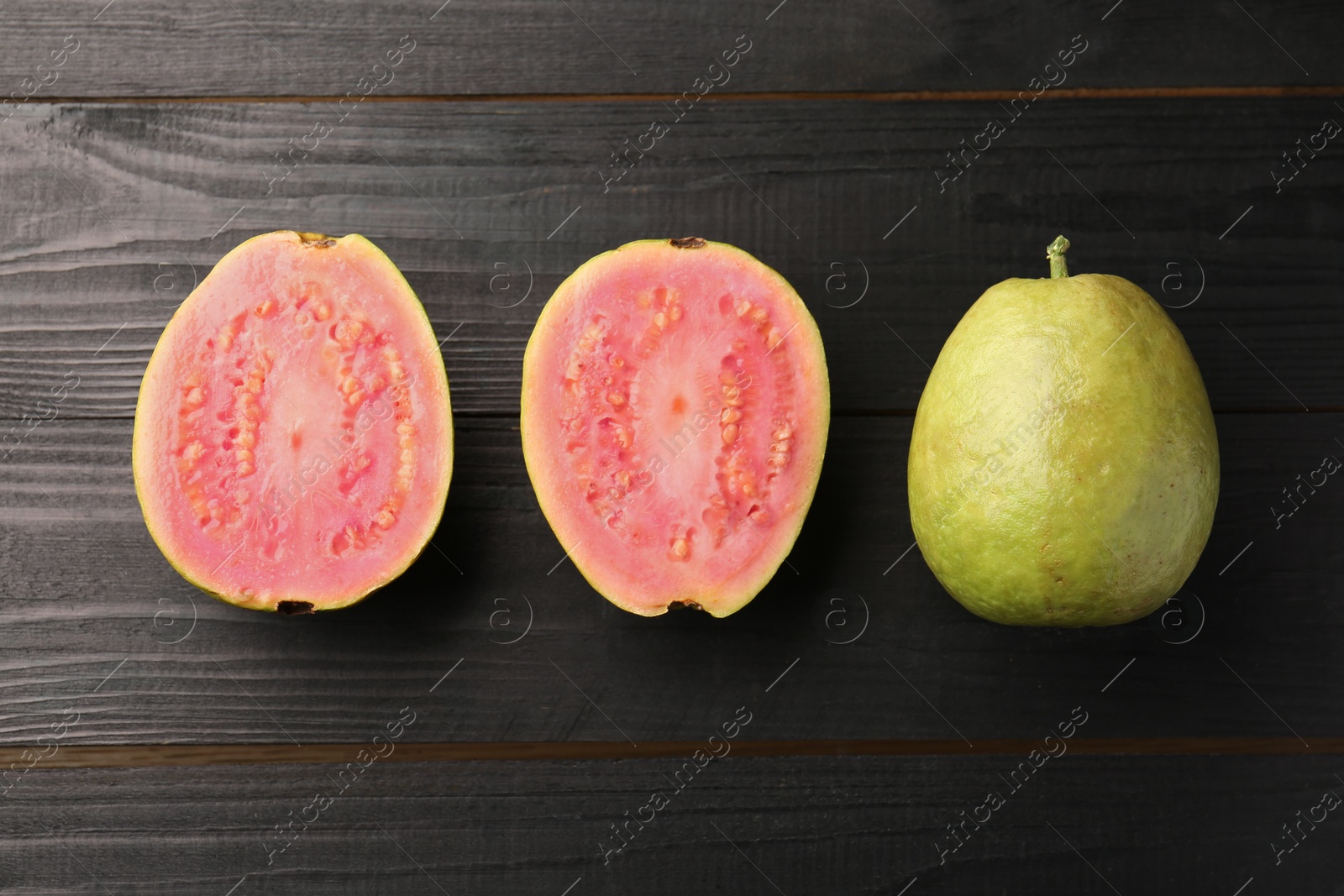 Photo of Fresh whole and cut guava fruits on black wooden table, flat lay