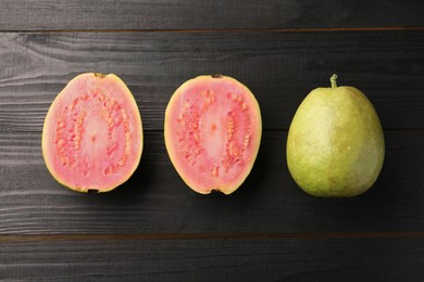 Photo of Fresh whole and cut guava fruits on black wooden table, flat lay