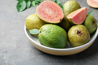 Fresh whole and cut guava fruits in bowl on grey textured table, closeup