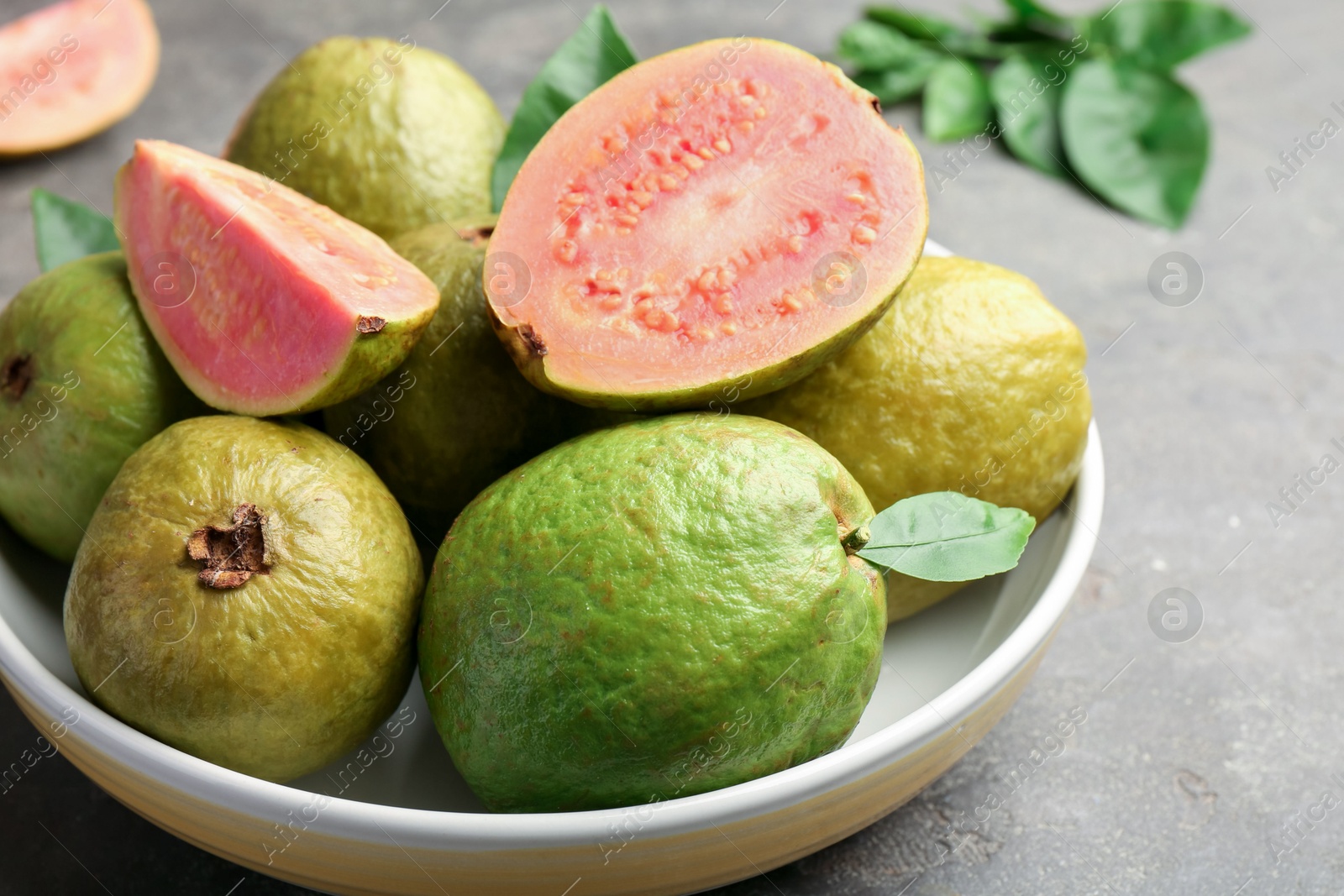 Photo of Fresh whole and cut guava fruits in bowl on grey textured table, closeup