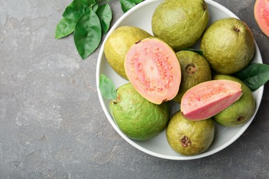 Fresh whole and cut guava fruits in bowl on grey textured table, top view. Space for text