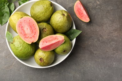 Photo of Fresh whole and cut guava fruits in bowl on grey textured table, top view. Space for text