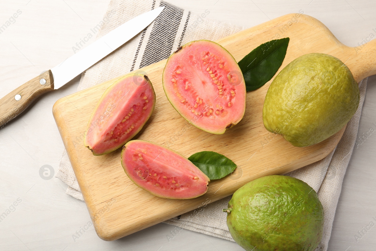 Photo of Fresh whole and cut guava fruits with knife on white wooden table, flat lay