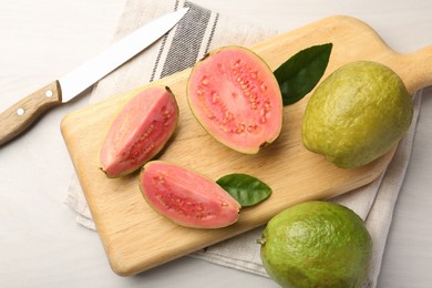 Photo of Fresh whole and cut guava fruits with knife on white wooden table, flat lay