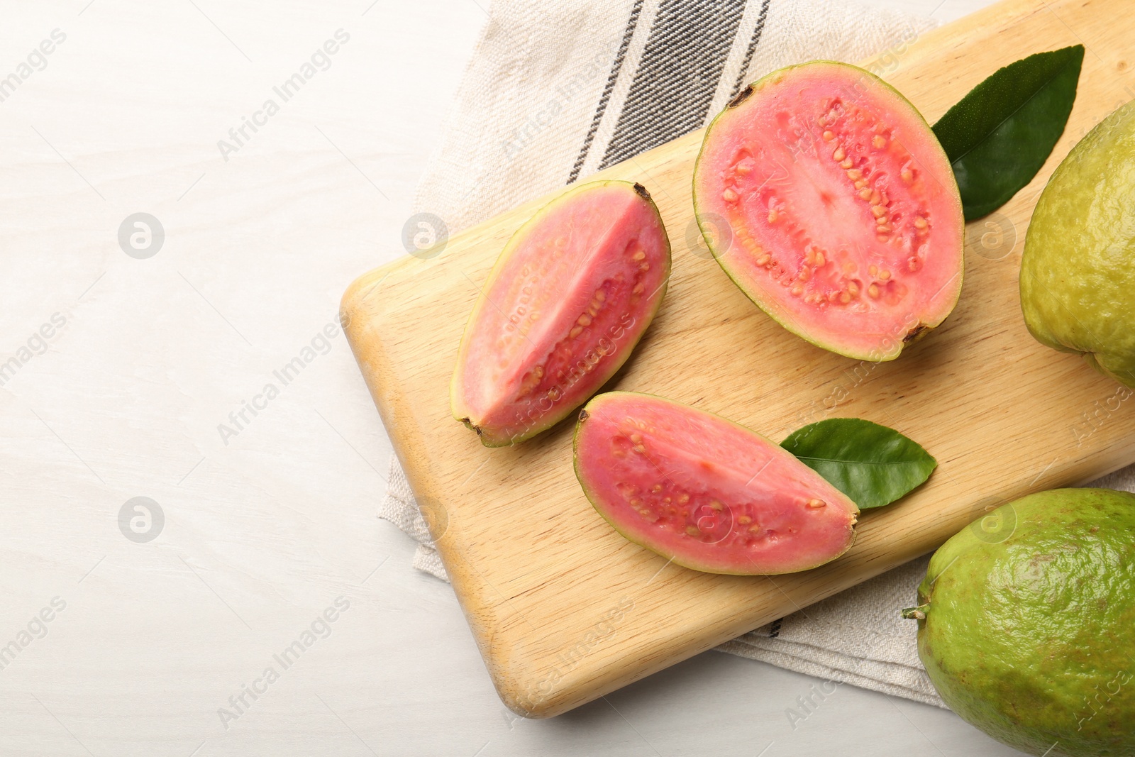 Photo of Fresh whole and cut guava fruits on white wooden table, top view. Space for text