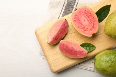 Fresh whole and cut guava fruits on white wooden table, top view. Space for text