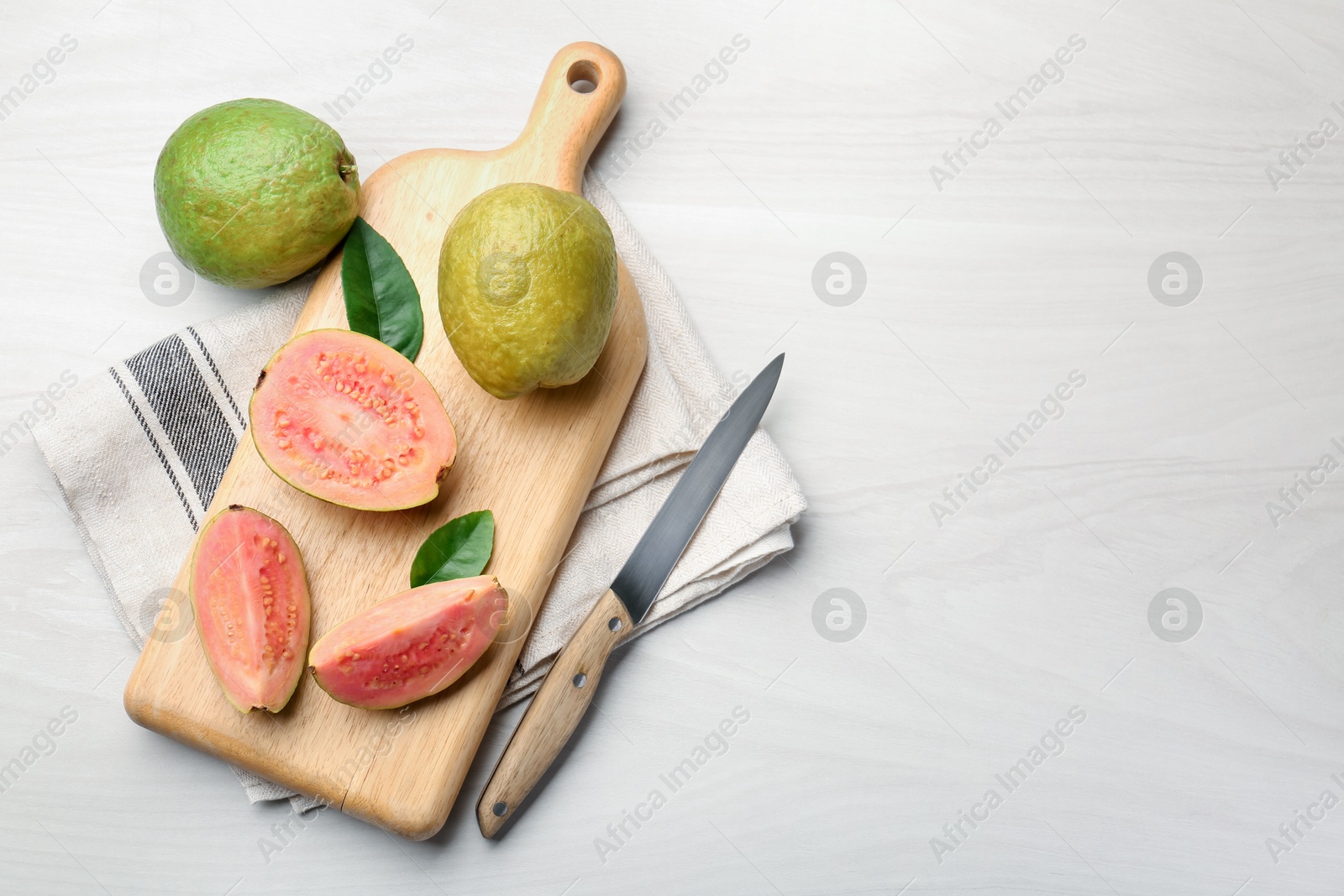 Photo of Fresh whole and cut guava fruits with knife on white wooden table, flat lay. Space for text