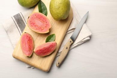 Fresh whole and cut guava fruits with knife on white wooden table, flat lay