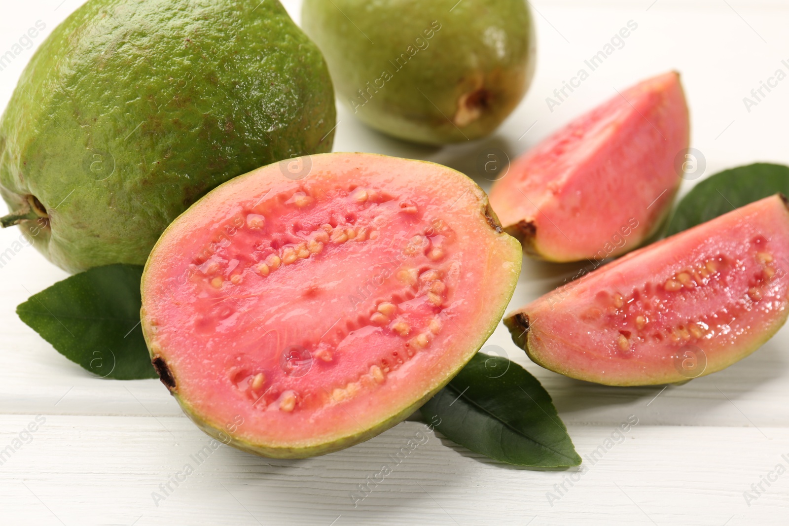 Photo of Fresh whole and cut guava fruits on white wooden table, closeup