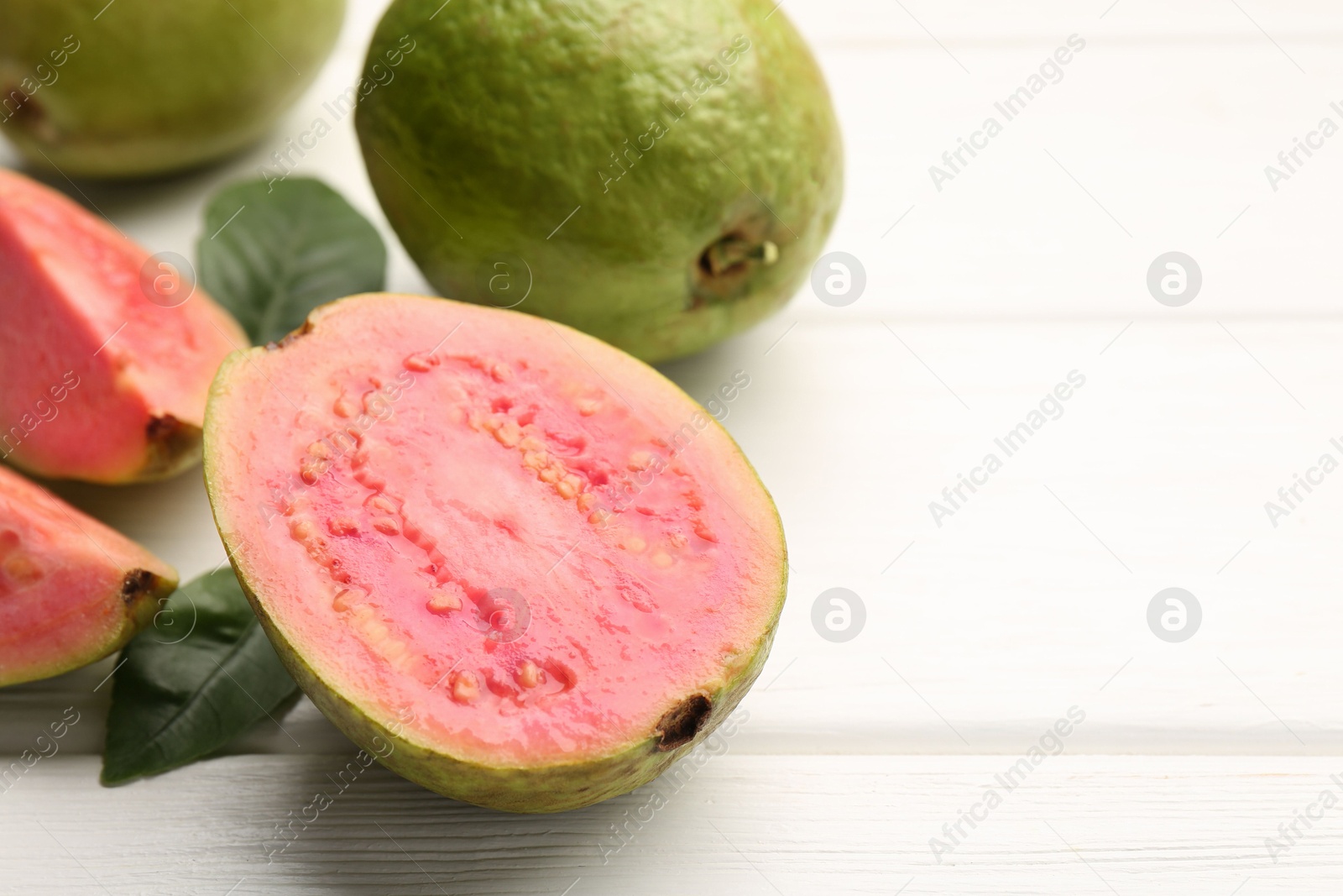 Photo of Fresh whole and cut guava fruits on white wooden table, closeup. Space for text