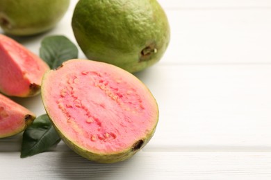 Photo of Fresh whole and cut guava fruits on white wooden table, closeup. Space for text