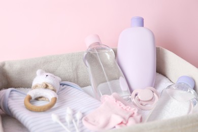 Photo of Baby oil and bath accessories in basket on light pink background, closeup