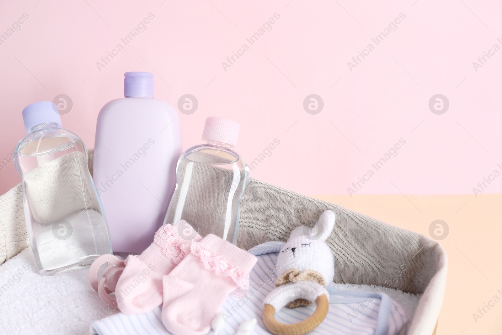 Photo of Baby oil and bath accessories in basket on color background, closeup. Space for text