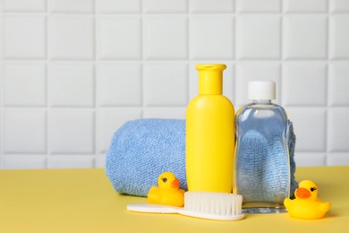 Photo of Baby oil and bath accessories on yellow table. Space for text