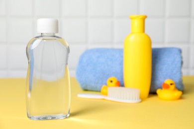 Photo of Baby oil and bath accessories on yellow table, selective focus