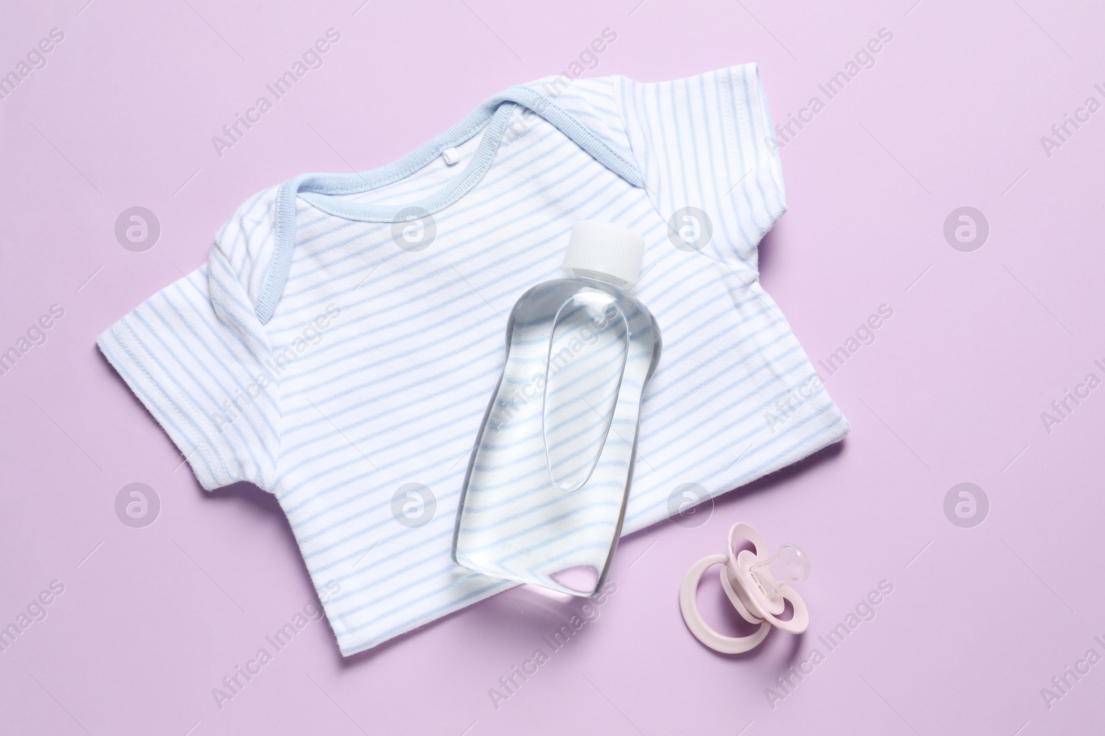 Photo of Baby oil, pacifier and onesie on lilac background, top view