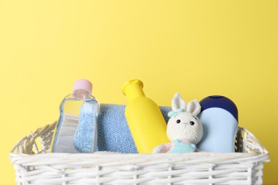 Photo of Baby oil and bath accessories in basket on yellow background, closeup