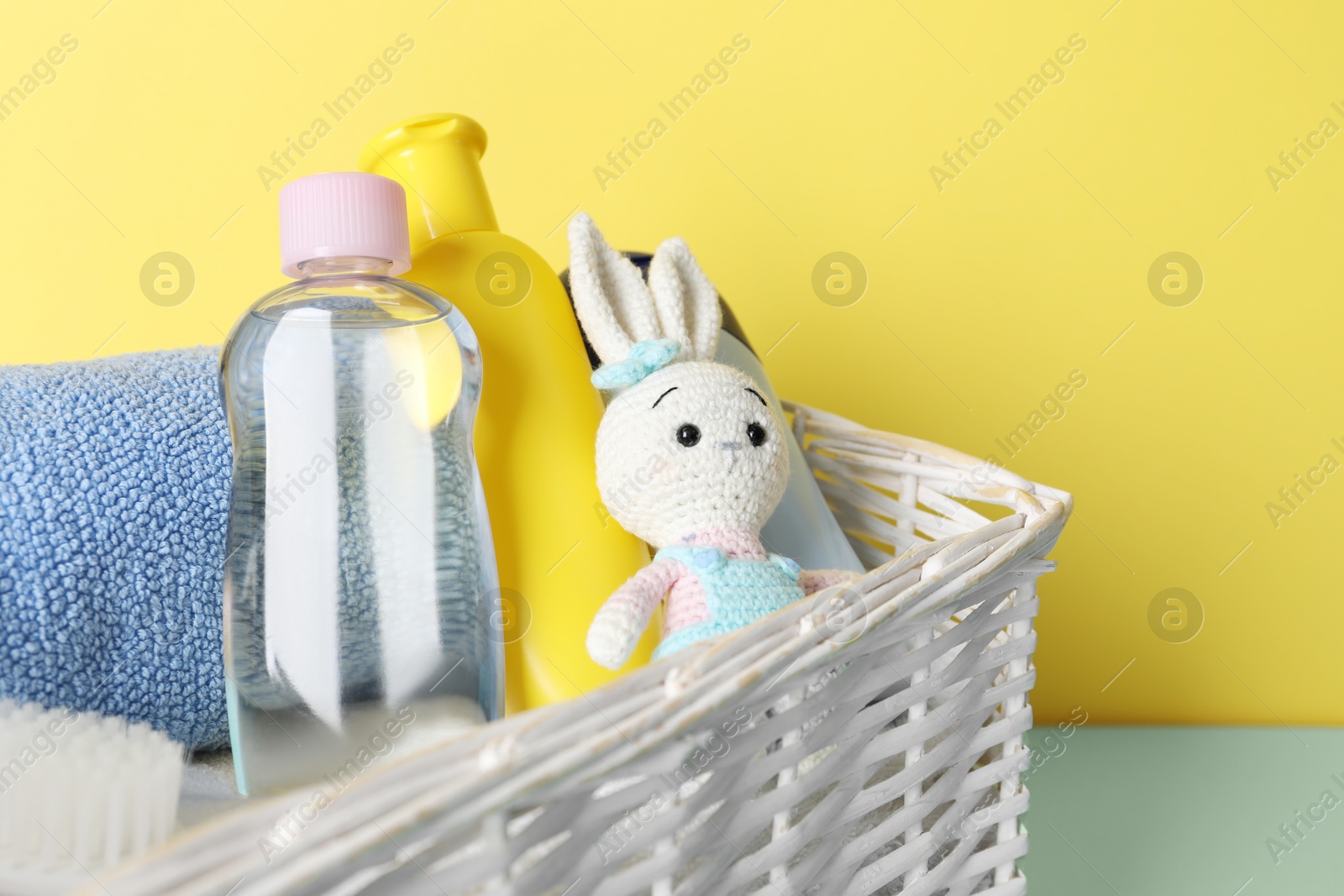 Photo of Baby oil and bath accessories in basket on color background, closeup