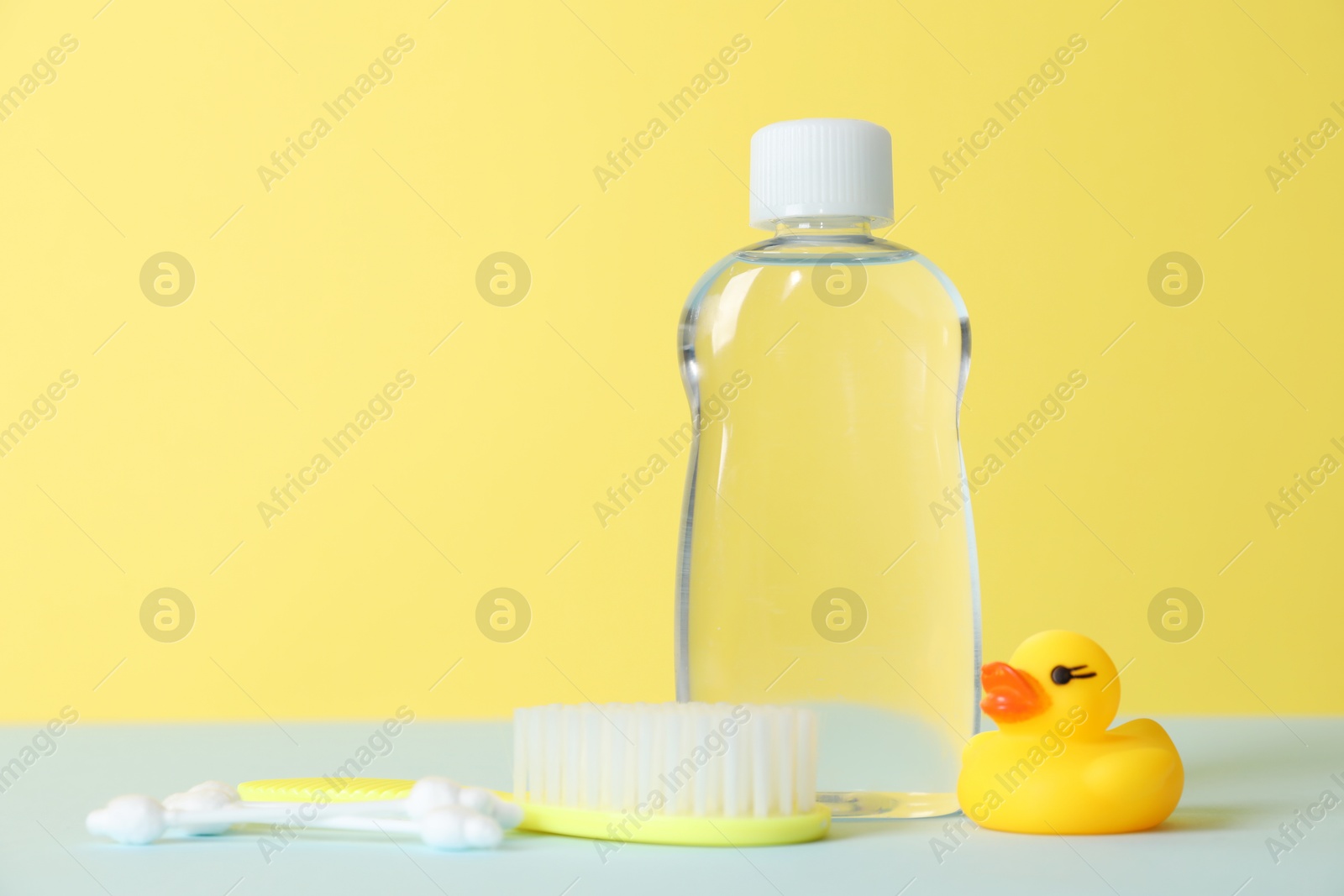 Photo of Baby oil, rubber duck, brush and cotton swabs on color background. Space for text