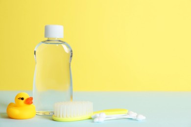 Photo of Baby oil, rubber duck, brush and cotton swabs on color background. Space for text