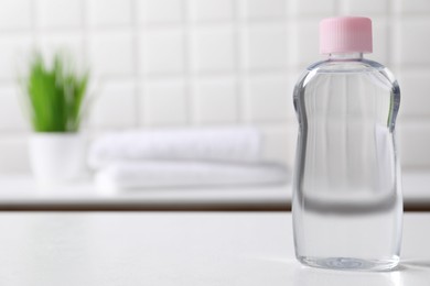 Photo of Baby oil in bottle on white table against blurred background. Space for text