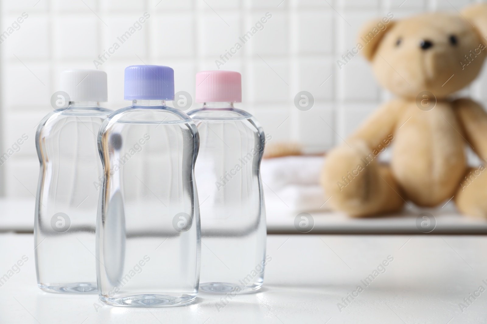 Photo of Baby oil in bottles on white table against blurred background. Space for text