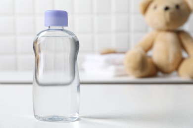 Photo of Baby oil in bottle on white table against blurred background. Space for text