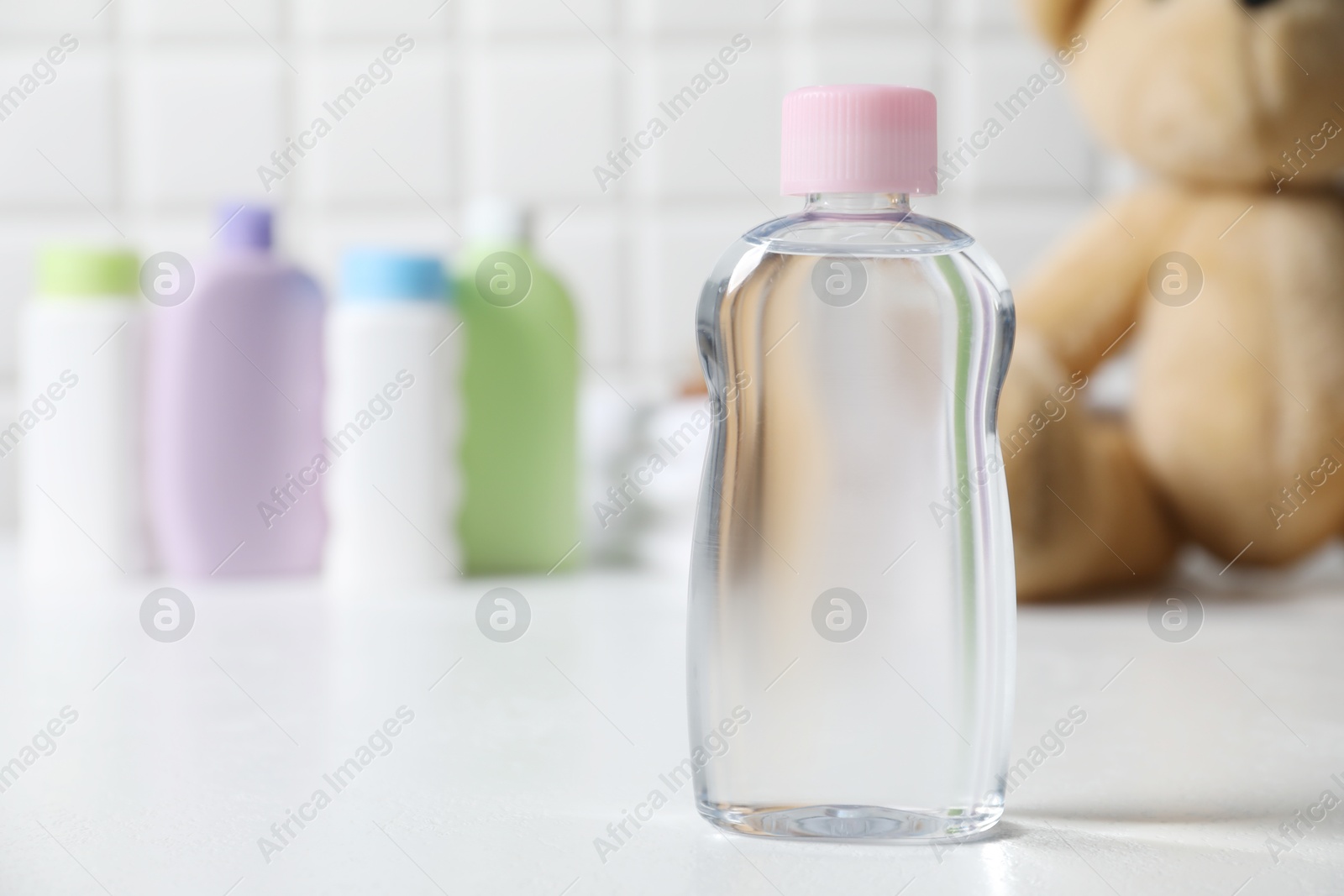 Photo of Baby oil in bottle on white table against blurred background. Space for text