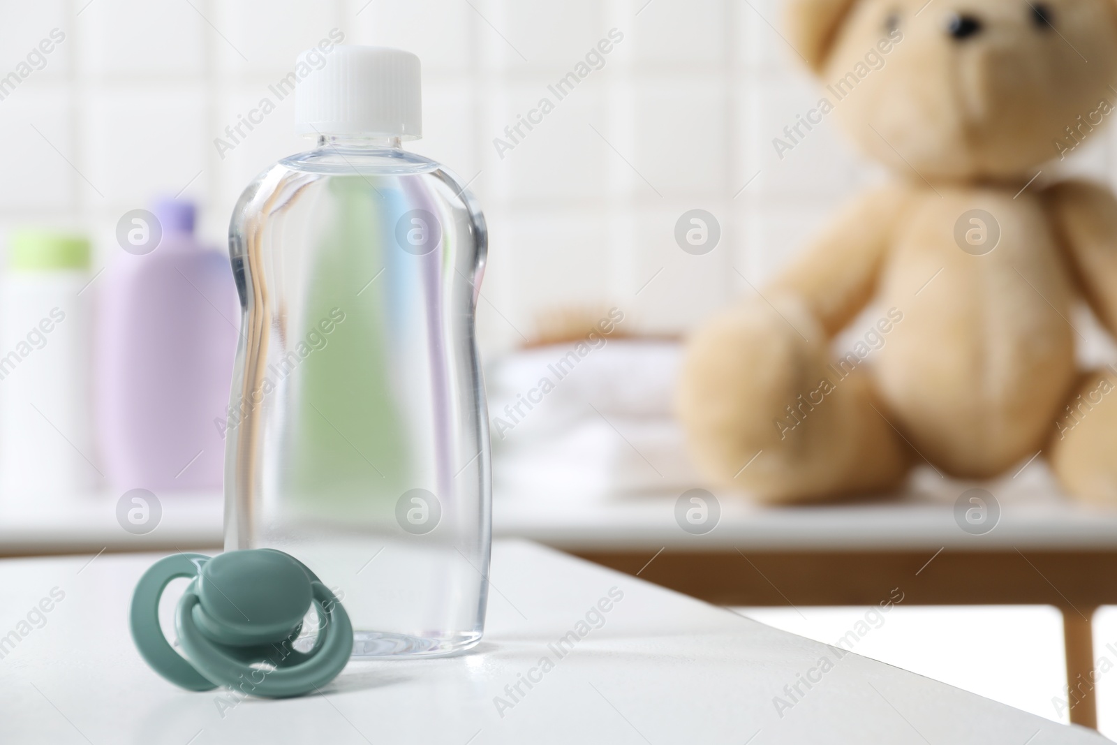 Photo of Baby oil in bottle and pacifier on white table against blurred background. Space for text