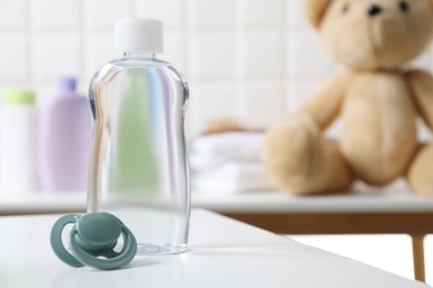 Photo of Baby oil in bottle and pacifier on white table against blurred background. Space for text