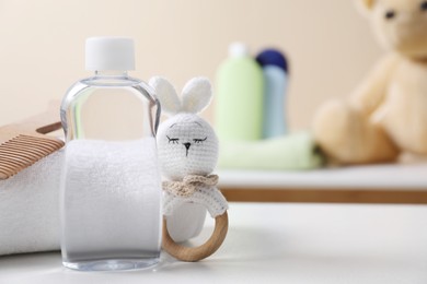 Photo of Baby oil in bottle, towel, comb and toy bunny on white table against blurred background. Space for text