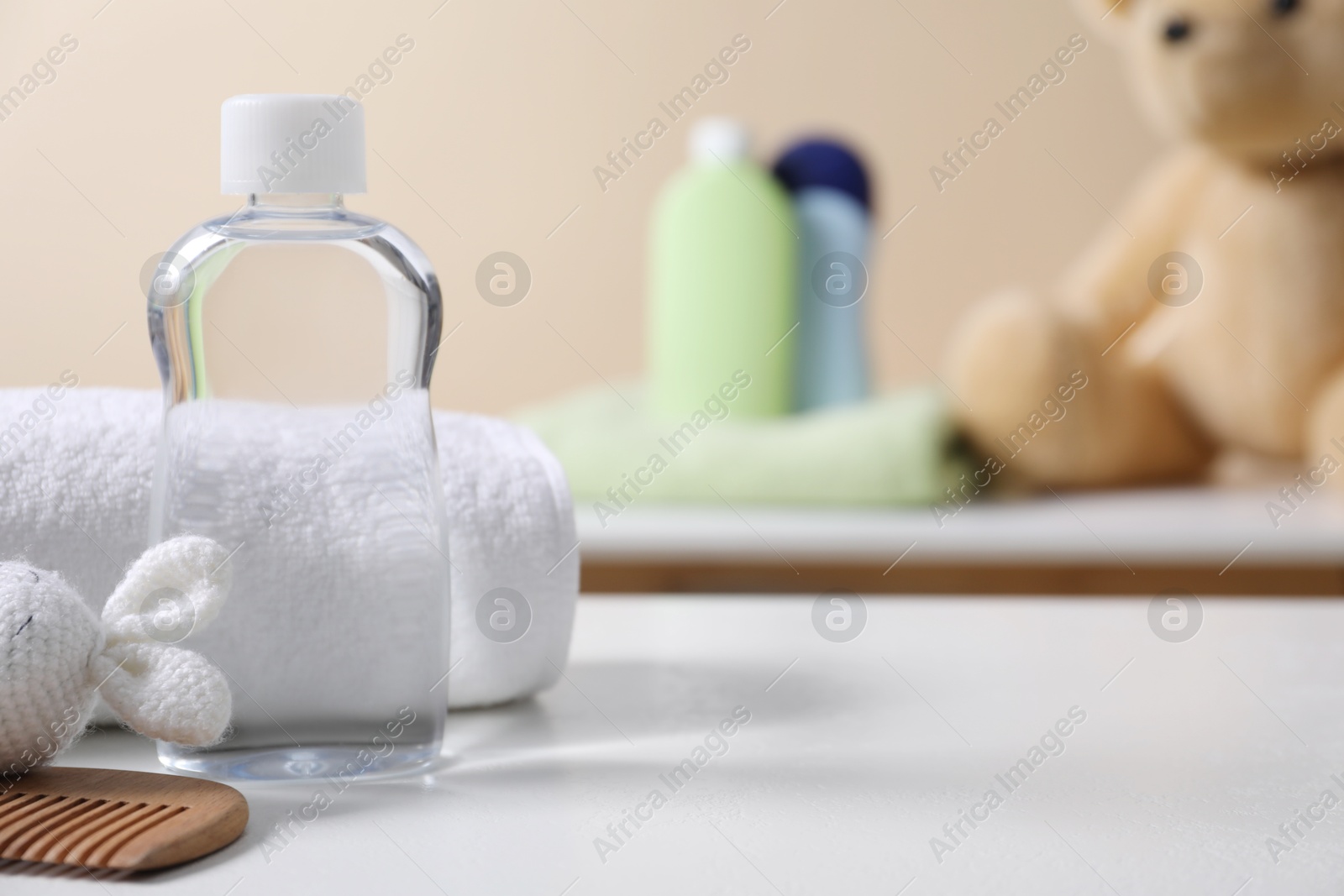 Photo of Baby oil in bottle, towel, comb and toy bunny on white table against blurred background. Space for text