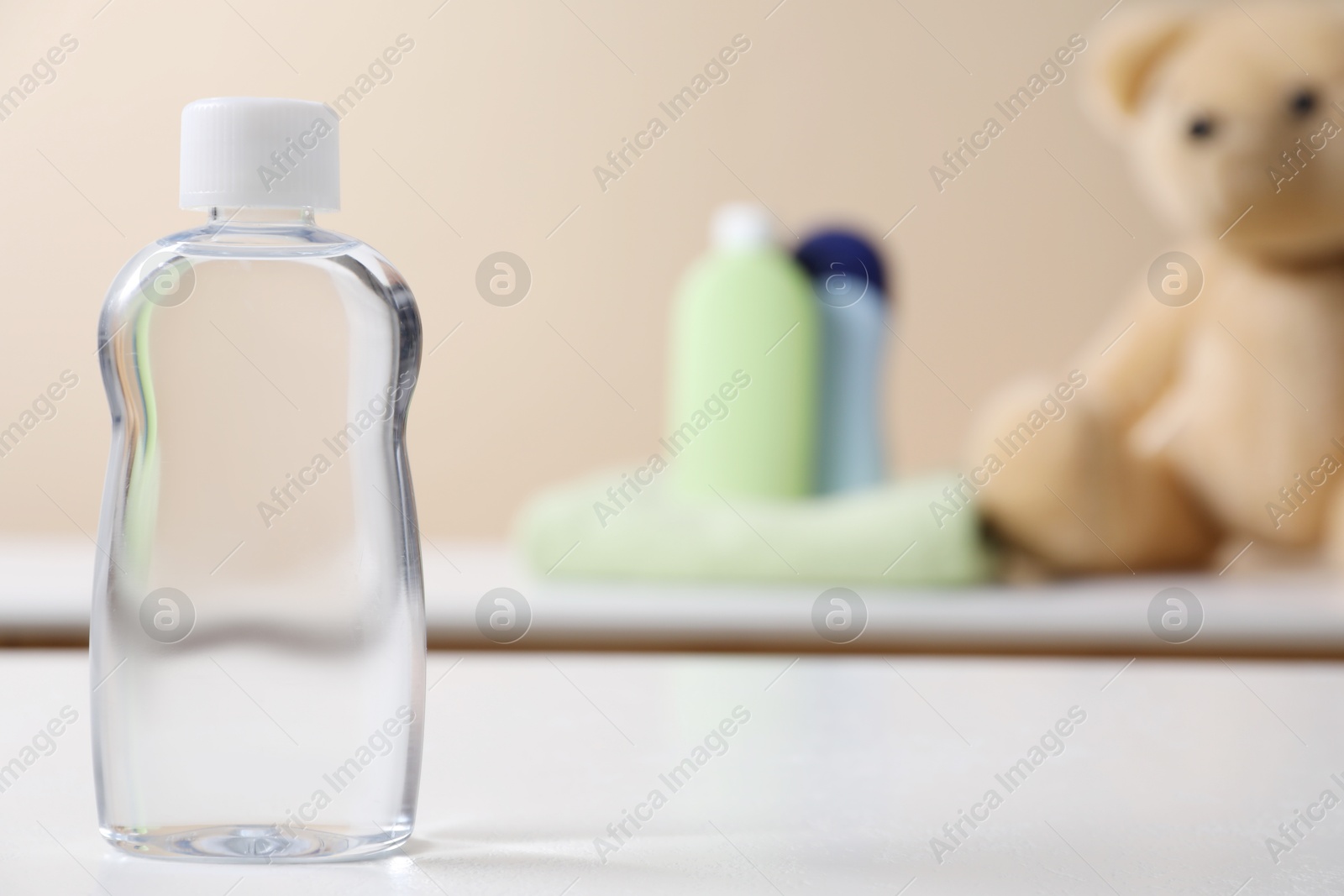 Photo of Baby oil in bottle on white table against blurred background. Space for text