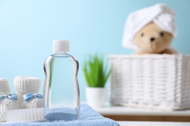 Photo of Baby oil in bottle, booties and brush on towel against blurred background