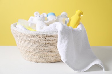 Photo of Baby oil and other toiletries in basket on white table against yellow background