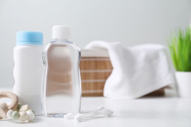 Photo of Baby oil, powder, cotton swabs and teether on white table against blurred background. Space for text