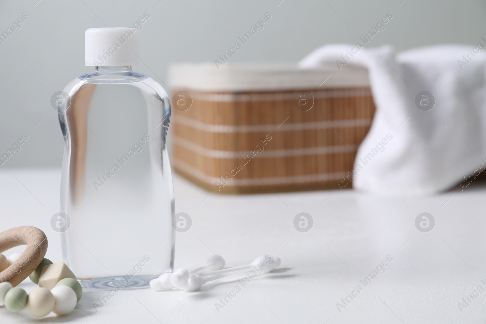 Photo of Baby oil, cotton swabs and teether on white table against blurred background. Space for text