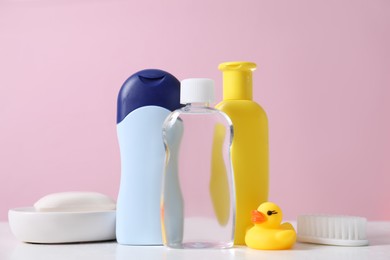 Photo of Baby oil and other toiletries on white table against pink background