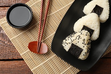 Photo of Rice balls (onigiri), soy sauce and chopsticks on wooden table, flat lay. Traditional Japanese dish