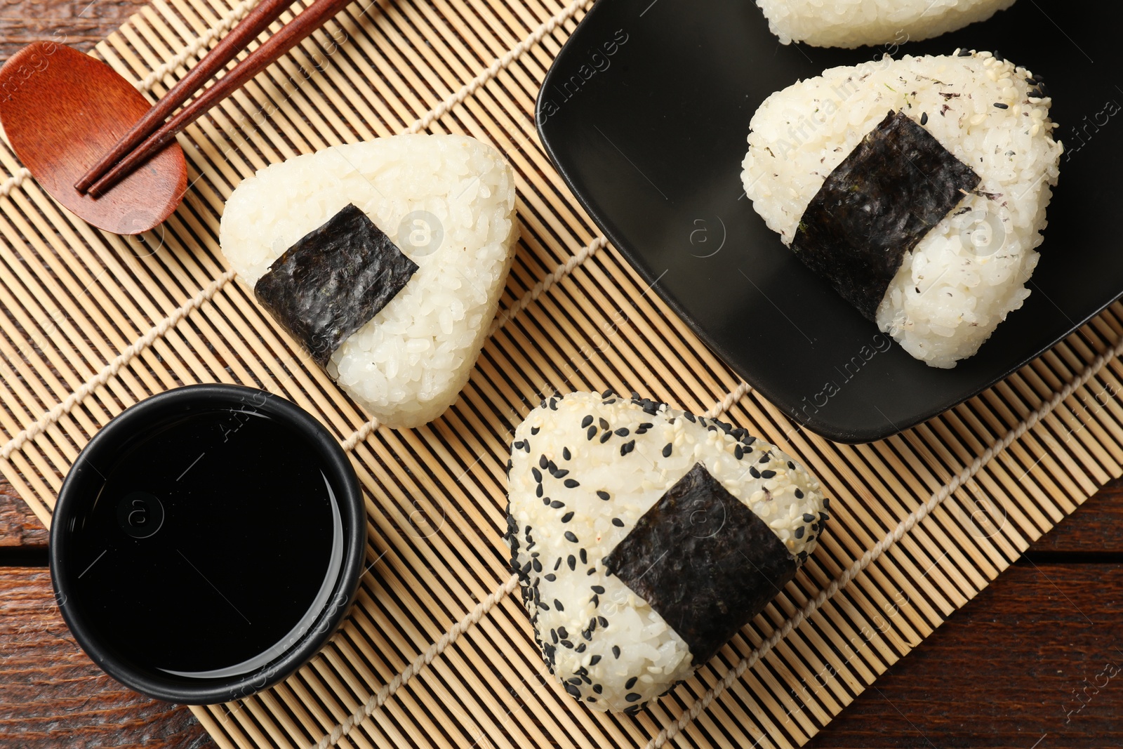 Photo of Rice balls (onigiri), soy sauce and chopsticks on wooden table, flat lay. Traditional Japanese dish