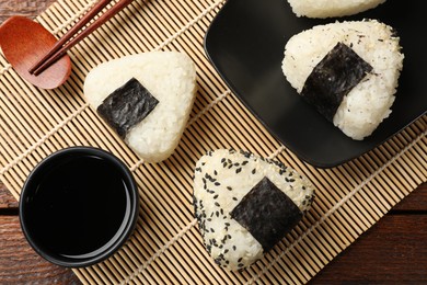 Photo of Rice balls (onigiri), soy sauce and chopsticks on wooden table, flat lay. Traditional Japanese dish