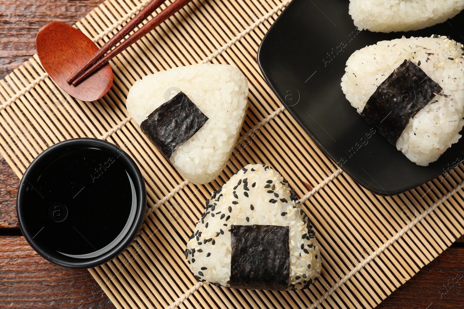 Photo of Rice balls (onigiri), soy sauce and chopsticks on wooden table, flat lay. Traditional Japanese dish