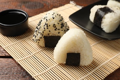 Photo of Rice balls (onigiri) and soy sauce on wooden table, closeup. Traditional Japanese dish